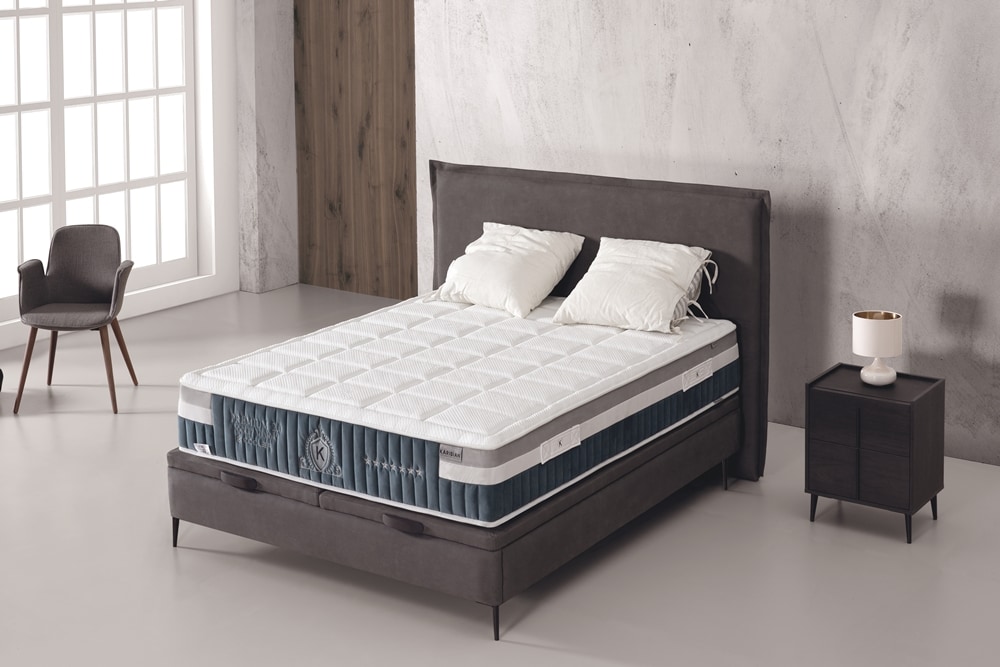 Un dormitorio moderno con una cama tapizada en color gris con un Colchón Karibian modelo Premium 2.0 COOLER, ropa de cama blanca y una mesa auxiliar minimalista con una lámpara COOLER.
