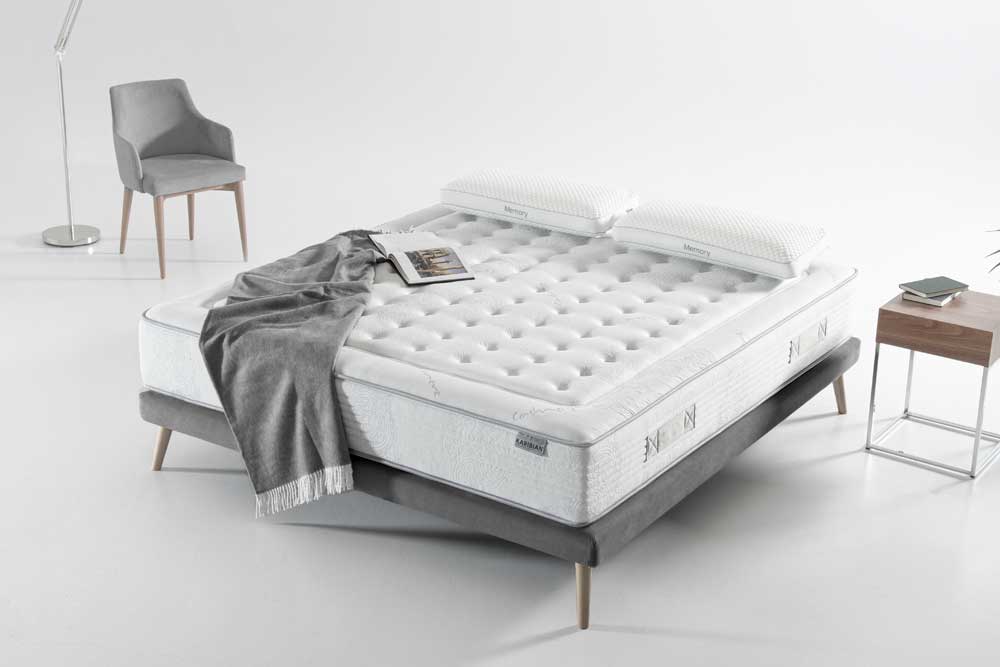 Dormitorio moderno con una cama Colchón Karibian modelo Solid Firm cuidadosamente hecha, una manta gris cubierta en una esquina y una revista encima, junto a una mesa y una silla auxiliar minimalistas