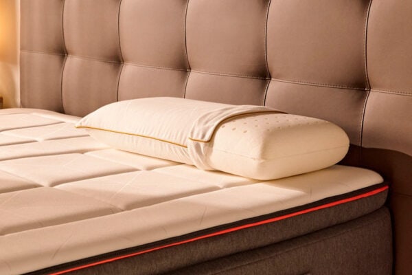 Almohada viscoelástica Bela KHAMA sobre un colchón lujoso con costuras detalladas.