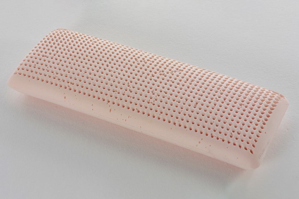 Goma de borrar rectangular de color rosa con superficie texturizada sobre fondo blanco, que recuerda a un diseño de Almohada Viscoelástica Fisio.