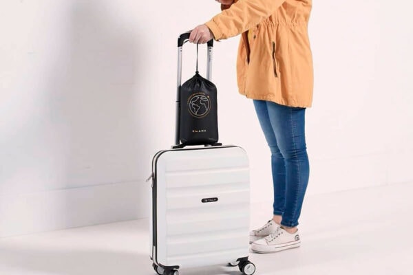 Una persona de pie con una maleta blanca y sosteniendo un bolso Almohada Travel KHAMA negro.