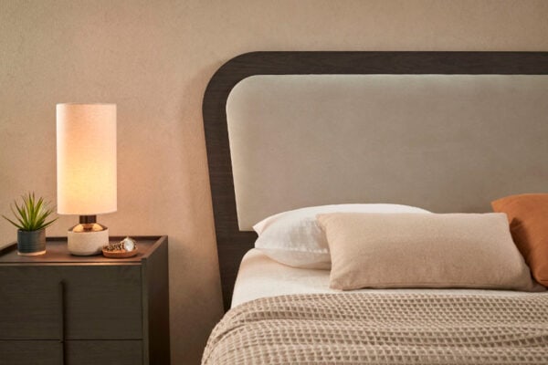 Frase con nombre de producto reemplazado: Una acogedora escena de dormitorio con una cama cuidadosamente hecha con un Cabecero Astoria Soft, una mesita de noche de madera y una lámpara de mesa iluminada.