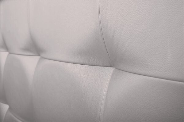 Primer plano de un sofá de cuero blanco con detalle de costuras, con diseño de Cabecero modelo Duomo al suelo.