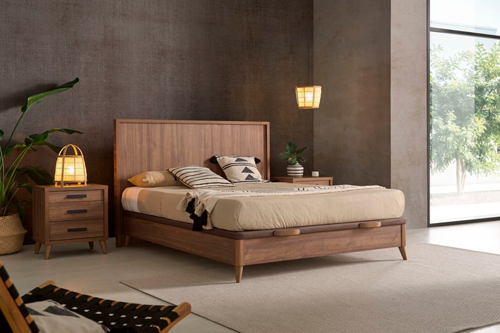 Un dormitorio moderno con cama de madera, mesitas auxiliares e iluminación tenue, con una combinación de colores neutros y un gran ventanal. La pieza central es el modelo Kiara cabecero añadiendo un toque elegante.