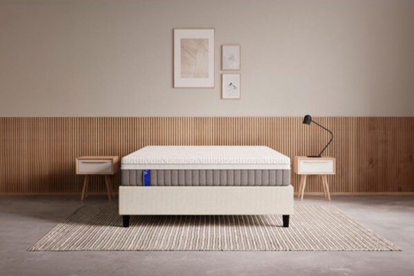 Interior de dormitorio minimalista con una moderna cama Colchón EMMA Body Adapt Hybrid, dos elegantes mesas auxiliares, una lámpara de pie y obras de arte enmarcadas en la pared.