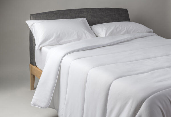 Una cama cuidadosamente hecha con ropa de cama Nordico de fibra Aloe Vera y una cabecera gris.