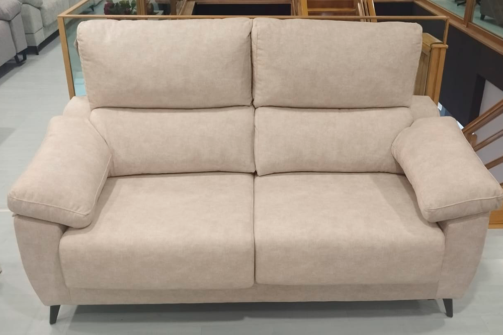 Una Sofá Yaiza (copia) de dos plazas con respaldos acolchados y reposabrazos descansa sobre un suelo claro en una sala de exposición de muebles.